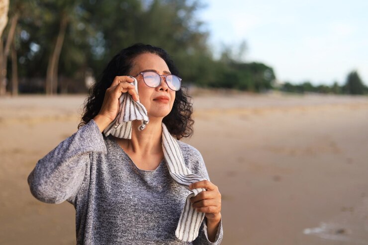 A woman wearing glasses and a sweater speaks on the phone, discussing Summer to Monsoon Skin Rashes.